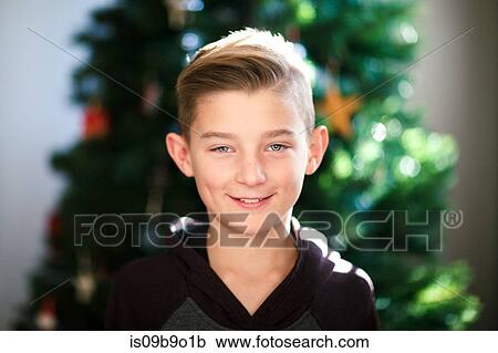 Stock Image - Portrait of boy, Christmas tree in background. Fotosearch