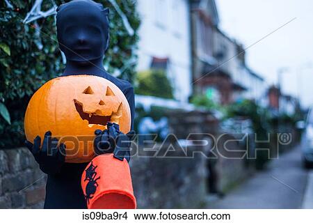 Picture - Portrait of boy in halloween costume, holding pumpkin and trick or treat bucket. Fotosearch