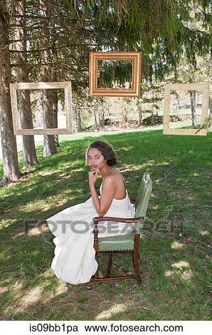 Stock Image - Portrait of bride wearing wedding dress, sitting in chair, outdoors. Fotosearch