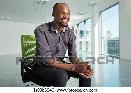 Stock Image - Portrait of businessman, sitting in chair, in empty office space. Fotosearch