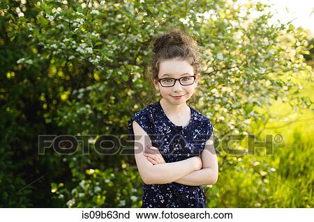 Stock Image - Portrait of girl wearing eye glasses in field with blossoming trees. Fotosearch