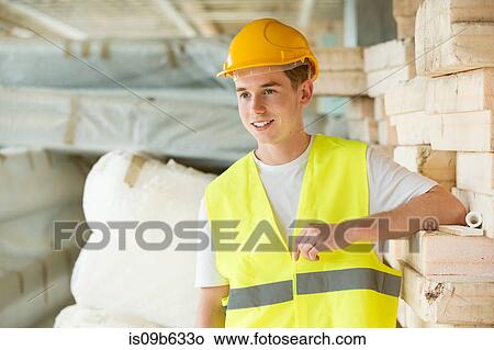 Picture - Portrait of man wearing hard hat and hi vis vest, standing beside building materials. Fotosearch