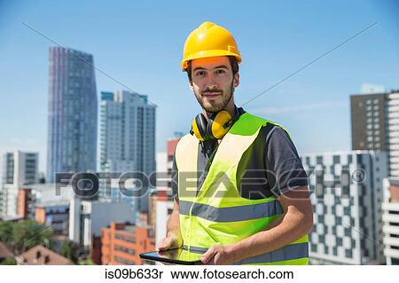 Stock Photography - Portrait of man wearing hard hat and hi vis vest, holding digital table, outdoors. Fotosearch