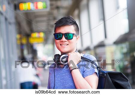 Stock Image - Portrait of man with headphone wearing sunglasses looking at camera smiling. Fotosearch