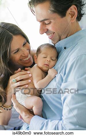 Stock Image - Portrait of mother and father, holding newborn baby boy, smiling. Fotosearch