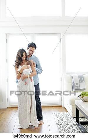 Stock Image - Portrait of mother and father, holding newborn baby boy, smiling. Fotosearch