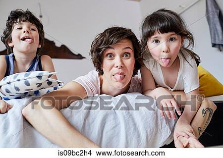 Portrait of mother, son and daughter, lying on bed, poking tongue out View Large Photo Image Picture - Portrait of mother, son and daughter, lying on bed, poking tongue out. Fotosearch