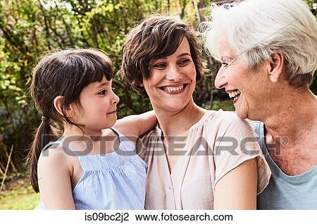 Stock Image - Portrait of senior woman with grown daughter and granddaughter, outdoors, smiling. Fotosearch