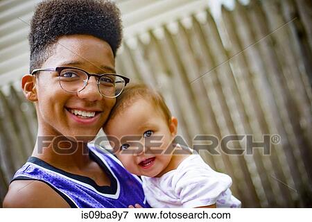 Portrait of teenage boy carrying baby girl in arms View Large Photo Image Stock Photo - Portrait of teenage boy carrying baby girl in arms. Fotosearch