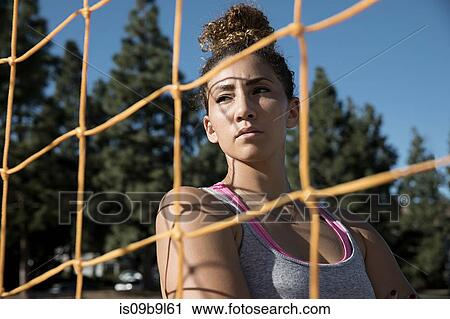 Stock Image - Portrait of woman behind football goal netting looking away. Fotosearch