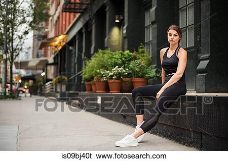 Stock Photograph - Portrait of woman wearing workout clothes sitting on wall looking at camera, New York, USA. Fotosearch