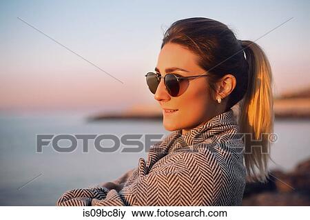 Stock Photo - Portrait of woman with ponytail wearing sunglasses looking away smiling, Odessa, Odeska Oblast, Ukraine, Eastern Europe. Fotosearch