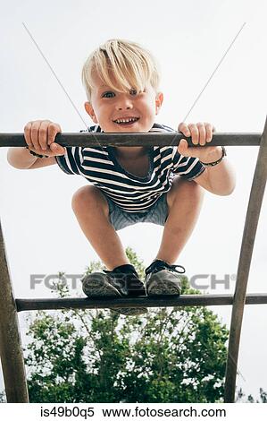Stock Photography - Portrait of young boy on playground climbing frame, low angle view. Fotosearch
