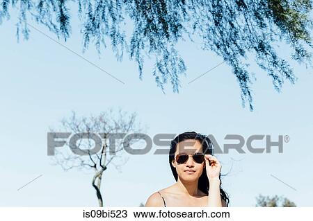 Portrait of young woman outdoors, adjusting sunglasses View Large Photo Image Stock Image - Portrait of young woman outdoors, adjusting sunglasses. Fotosearch