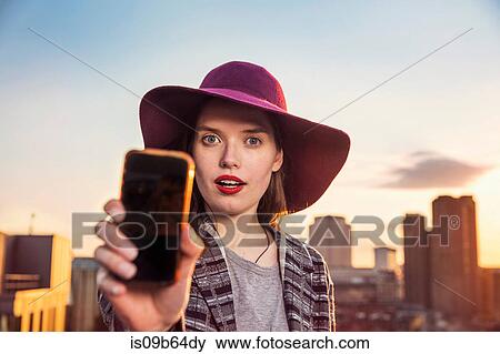 Portrait of young woman taking smartphone selfie at sunset roof party in London, UK View Large Photo Image Stock Photo - Portrait of young woman taking smartphone selfie at sunset roof party in London, UK. Fotosearch