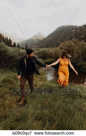 Stock Photo - Pregnant mid adult couple holding hands by rural river, Mineral King, California, USA. Fotosearch