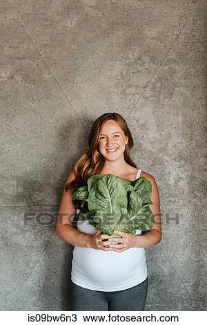 Stock Image - Pregnant woman holding up lettuce. Fotosearch