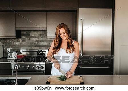 Stock Image - Pregnant woman preparing salad on cutting board in kitchen. Fotosearch