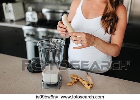 Stock Photo - Pregnant woman preparing smoothie in kitchen. Fotosearch