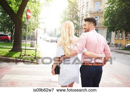 Stock Photo - Rear view of couple walking in street arms around each other. Fotosearch