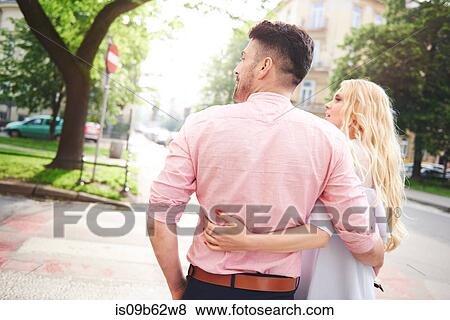 Stock Photo - Rear view of couple walking in street arms around each other. Fotosearch