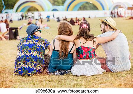 Rear view of friends sitting on grass at festival View Large Photo Image Stock Image - Rear view of friends sitting on grass at festival. Fotosearch