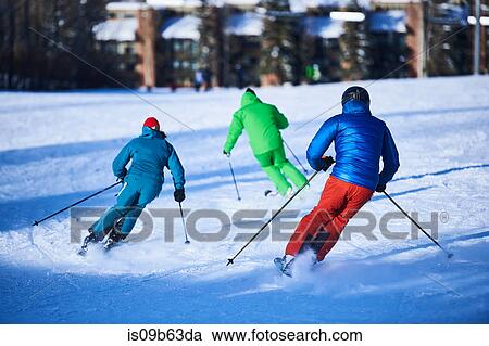 Stock Image - Rear view of male and female skiers skiing down snow covered ski slope, Aspen, Colorado, USA. Fotosearch