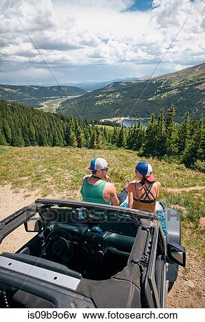 Stock Photo - Rear view of road trip couple sitting on four wheel convertible hood in Rocky mountains, Breckenridge, Colorado, USA. Fotosearch