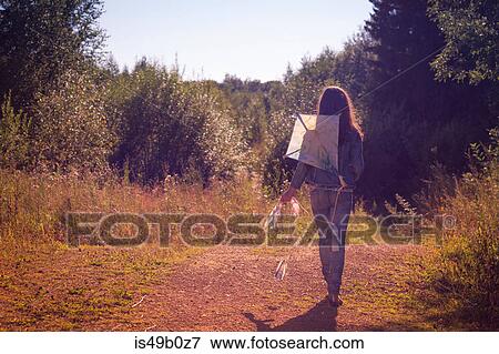 Stock Photo - Rear view of teenage girl walking with kite along dirt track. Fotosearch