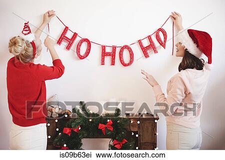 Rear view of two young women putting up christmas decorations on wall View Large Photo Image Stock Image - Rear view of two young women putting up christmas decorations on wall. Fotosearch