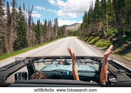 Stock Photo - Road trip couple driving convertible on rural highway with hands raised, Breckenridge, Colorado, USA. Fotosearch