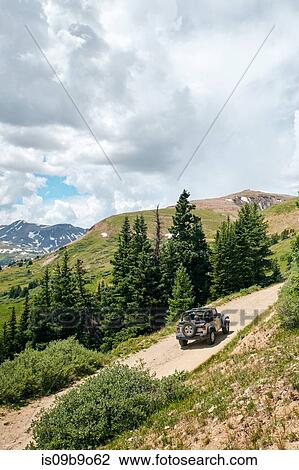 Stock Image - Road trip couple driving convertible off road vehicle on rural mountain road, Breckenridge, Colorado, USA. Fotosearch