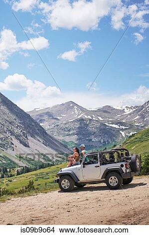 Picture - Road trip couple looking out at mountains from off road vehicle hood, Breckenridge, Colorado, USA. Fotosearch
