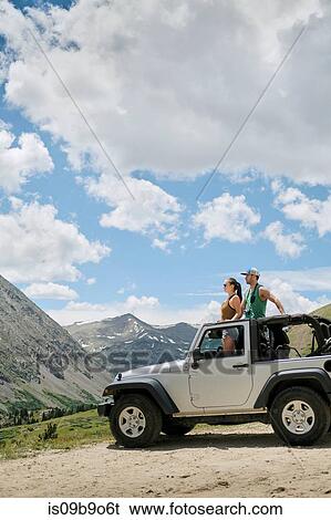 Stock Photograph - Road trip couple looking out from four wheel convertible in Rocky mountains, Breckenridge, Colorado, USA. Fotosearch