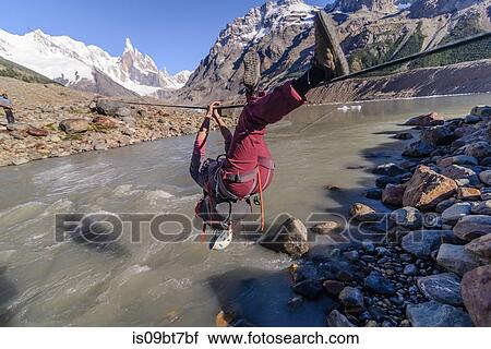 Stock Image - Rock climber sliding on rope over river, El Chaltn, south Patagonia, Argentina. Fotosearch