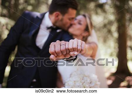 Stock Image - Romantic bride and groom kissing and showing wedding rings in woodland, selective focus on hands. Fotosearch