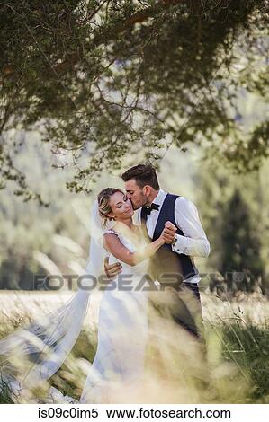 Stock Photography - Romantic groom kissing bride on cheek in woodland. Fotosearch