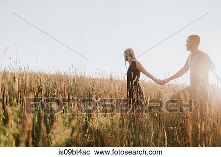 Romantic man and girlfriend holding hands in field of sunlit long grass View Large Photo Image Stock Image - Romantic man and girlfriend holding hands in field of sunlit long grass. Fotosearch