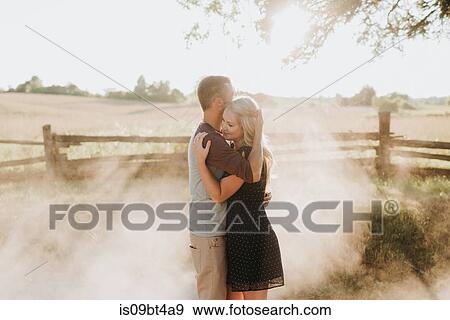 Stock Photo - Romantic man and girlfriend hugging on dusty dirt track at sunset. Fotosearch