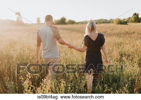 Romantic man and girlfriend strolling in field of sunlit long grass, rear view View Large Photo Image Stock Image - Romantic man and girlfriend strolling in field of sunlit long grass, rear view. Fotosearch