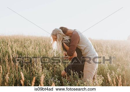 Stock Image - Romantic man hugging girlfriend in field of sunlit long grass. Fotosearch