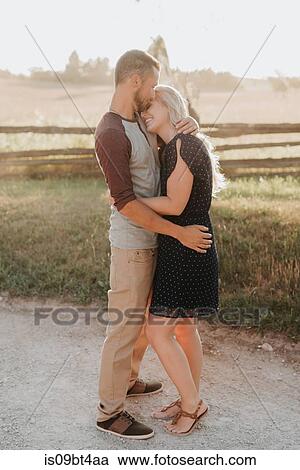 Stock Image - Romantic man kissing girlfriend on forehead on rural dirt track. Fotosearch