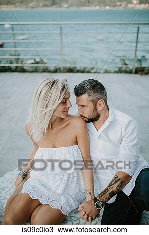 Stock Image - Romantic mid adult couple gazing at each other on lakeside, Stresa, Piemonte, Italy. Fotosearch