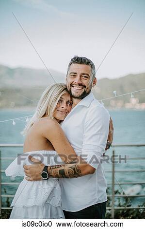 Stock Image - Romantic mid adult couple hugging on lakeside, portrait, Stresa, Piemonte, Italy. Fotosearch