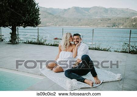 Stock Image - Romantic mid adult couple reclining on poolside, portrait, Stresa, Piemonte, Italy. Fotosearch