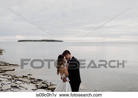 Stock Photo - Romantic young bride and groom hugging on lakeside on wedding day. Fotosearch