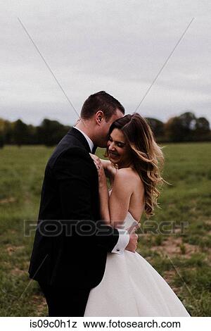 Romantic young bride and groom hugging in field View Large Photo Image Stock Photo - Romantic young bride and groom hugging in field. Fotosearch