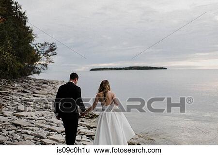 Romantic young bride and groom strolling along lakeside on wedding day View Large Photo Image Stock Photograph - Romantic young bride and groom strolling along lakeside on wedding day. Fotosearch