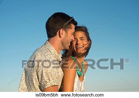 Romantic young couple laughing against blue sky View Large Photo Image Stock Image - Romantic young couple laughing against blue sky. Fotosearch