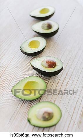 Stock Image - Row of halved avocado on wooden table, still life. Fotosearch